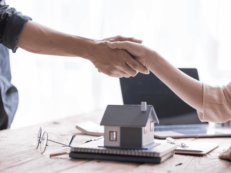 Immagine di due persone che si stringono la mano sopra un modello di casa, simbolo di accordo e coll.